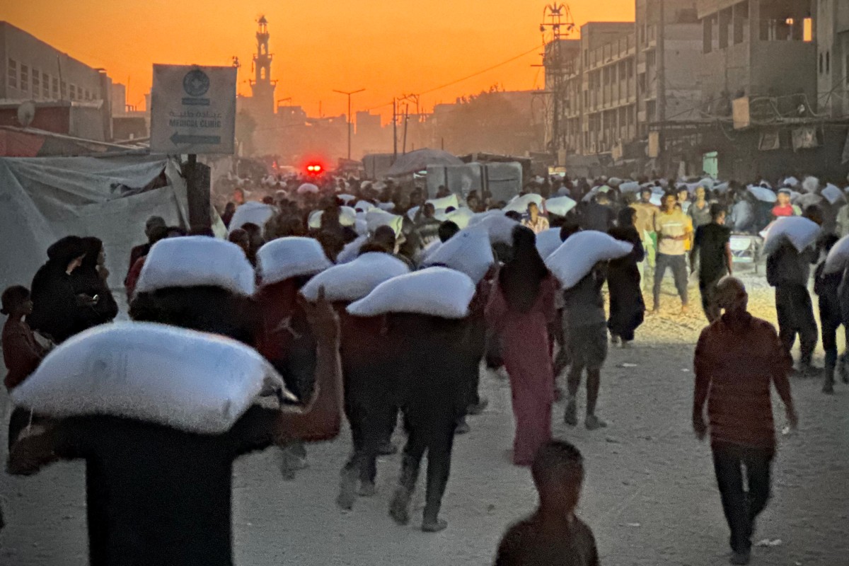 Men walk carrying sacks of flour that were taken from a raided truck carrying foodstuffs, in Khan Yunis in the southern Gaza Strip on July 22, 2025. (Photo by AFP)