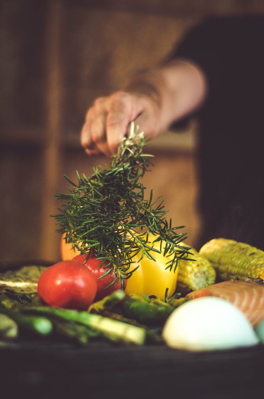Person putting rosemary into vegetable dish