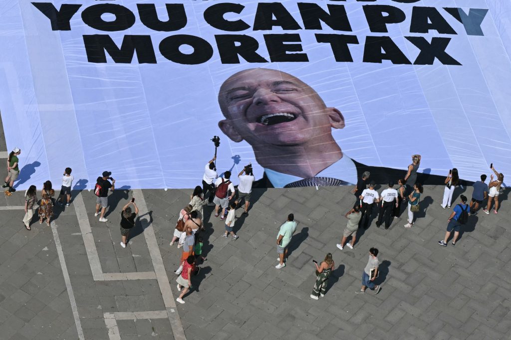 Activists of international environmental group Greenpeace deploy a giant banner displaying a picture of Jeff Bezos and reading "If you can rent Venice for your wedding you can pay more tax" at St Mark square in Venice yesterday. PHOTO: Stefano Rellandini / AFP