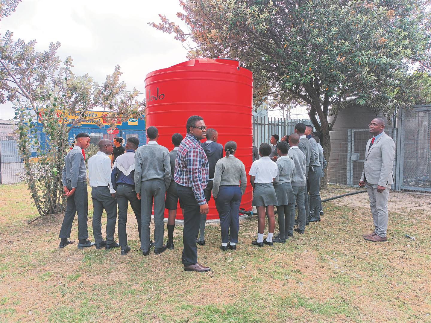Mbuzeli Mrwetyana from Clicks Group (in the striped shirt) together with the school principal Mzikabawo Mpisane (wearing a suit) are talking while learners are looking at the JoJo tank. 