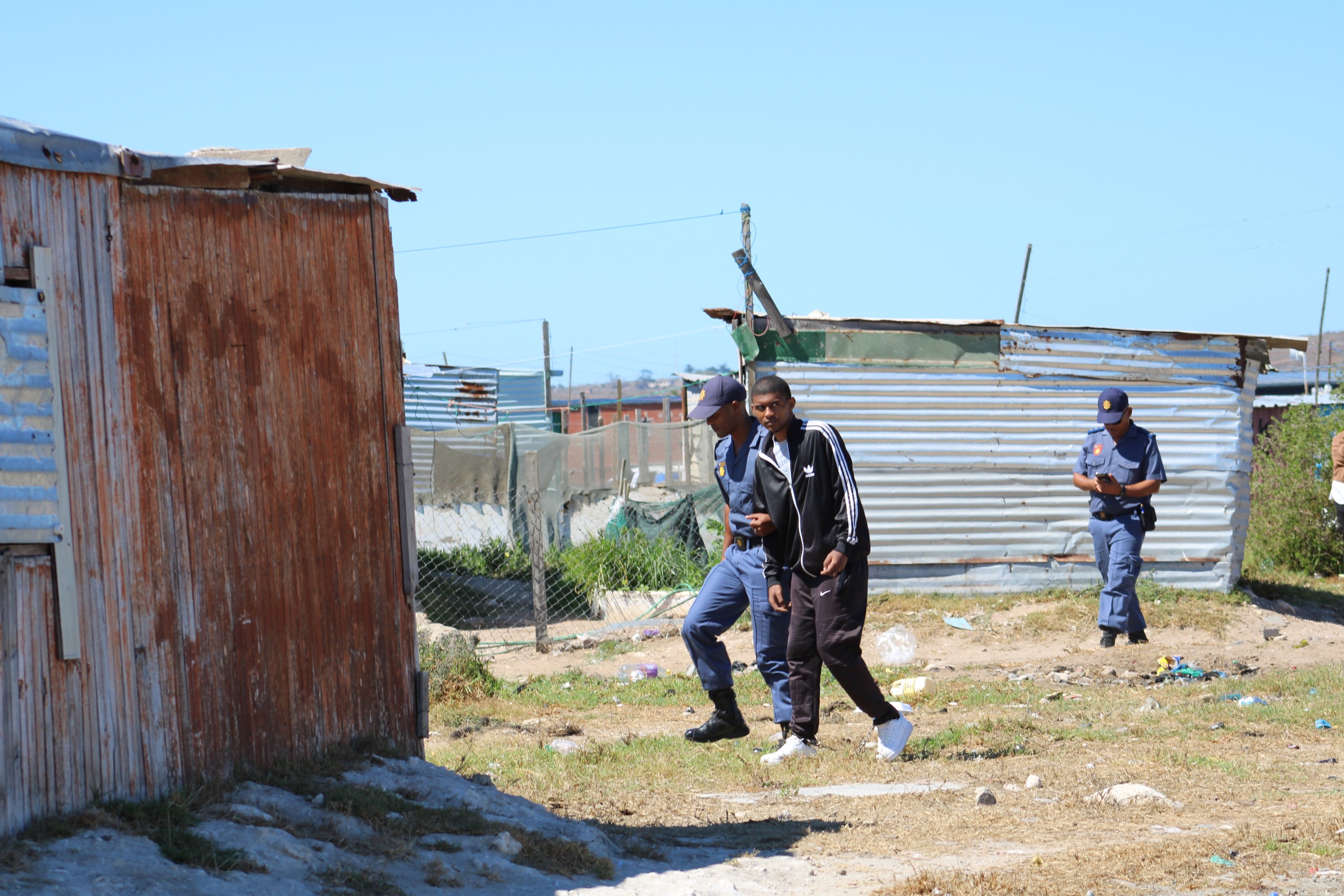 Steveno van Rhyn loop onder polisiebegeleiding in die Middelpos- informele nedersetting tydens 'n ter plaatse ondersoek as deel van die hooggeregshofsaak. Foto: Alida Buckle