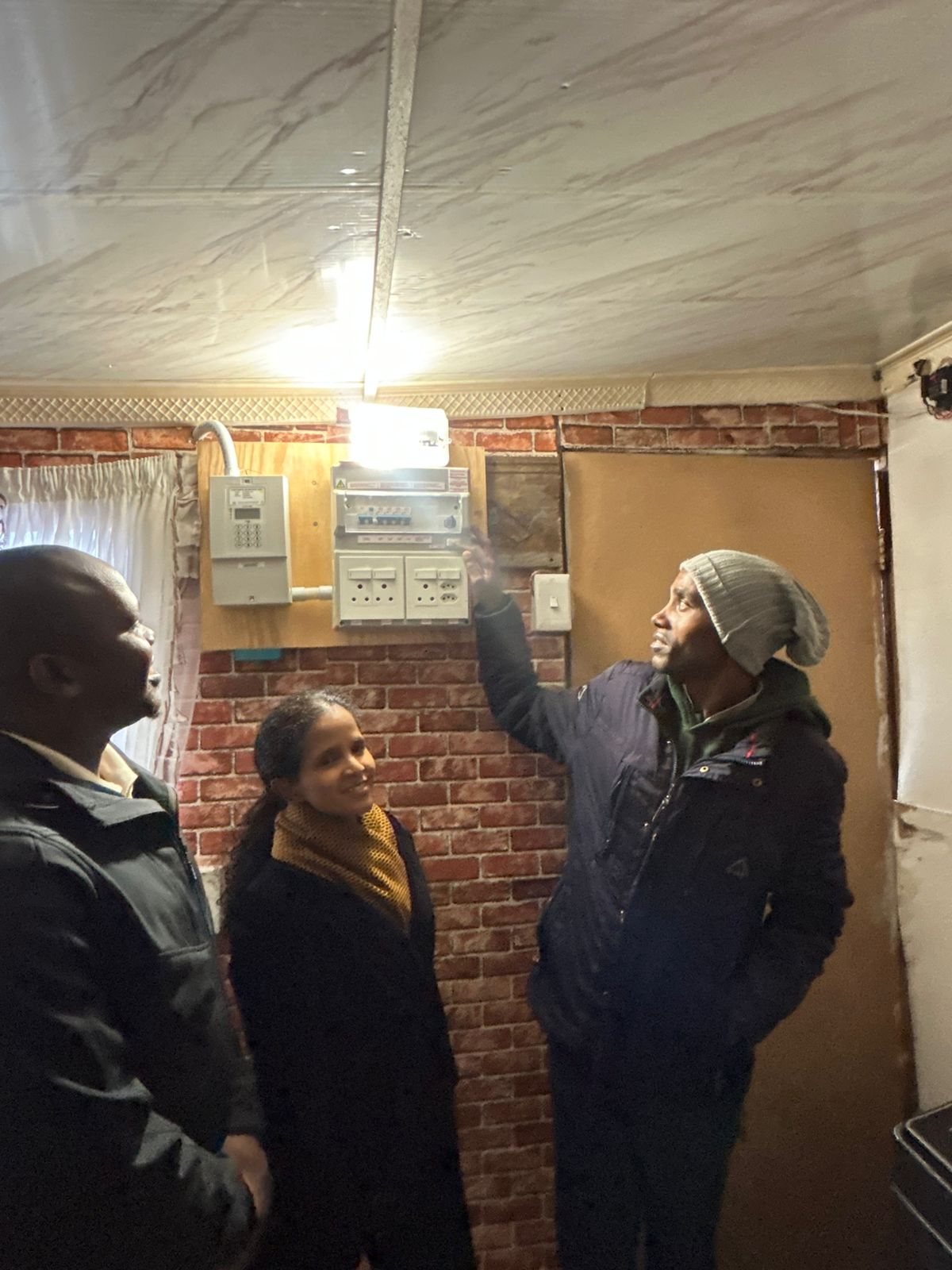 Shack owner Mlungisi Magwa switches on a light as the Mayco member for energy, Xanthea Limberg, and ward 51 councillor Lwazi Phakade look on. PHOTO: SUPPLIED