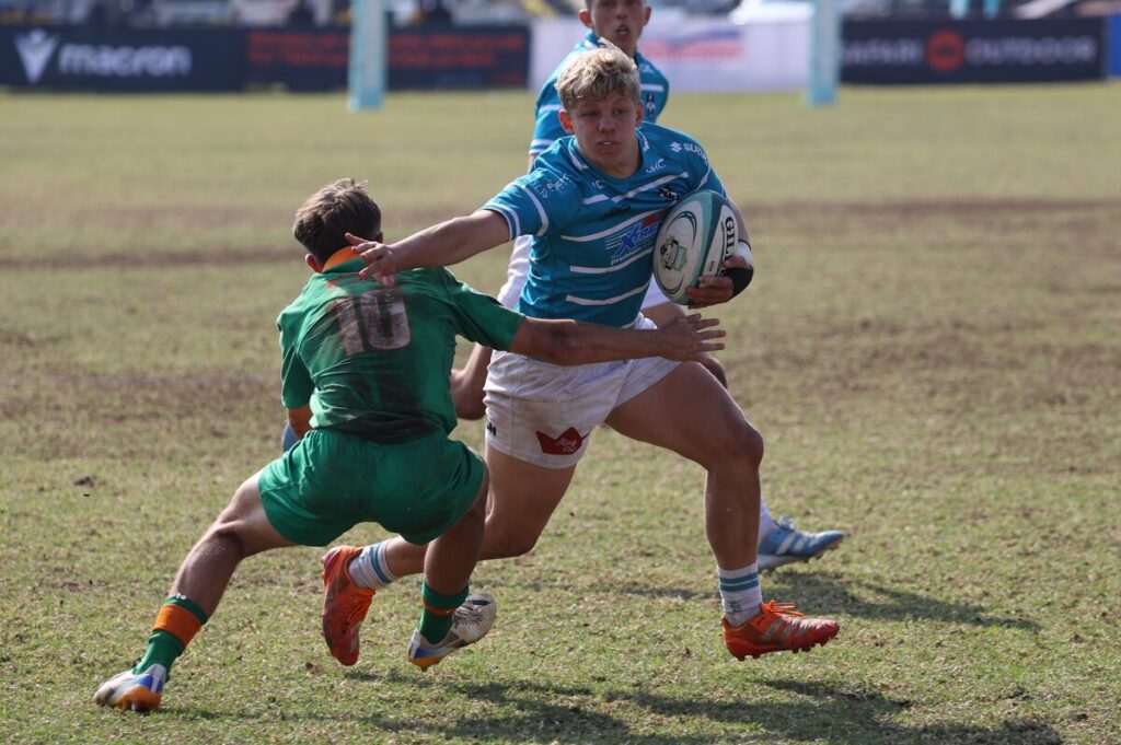 Keagan Knighton (met bal), binnesenter van die Hoërskool Garsfontein, probeer verby die Hoërskool Rustenburg se losskakel, Ricardo Enos, glip.