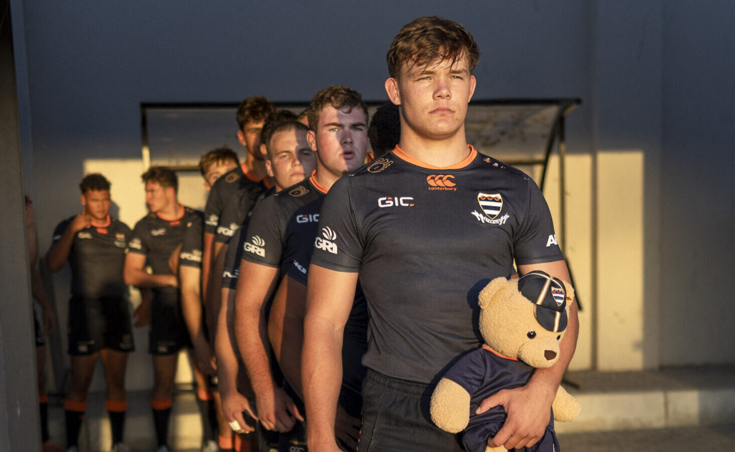 Grey College's captain and flanker Xander Smit (front), holding the mascot Tommix, prepares to lead his team on the field in Stellenbosch on March 29, 2025 ahead of their match against Noordheuwel during the Noord-Suid (North-South) rugby tournament. The cream of South African schools rugby talent gathered in the western Cape town of Stellenbosch this weekend to display their skills. Among the crowds were representatives from the major South African rugby franchises, trying to spot future stars and sign them. While many observers point to huge forwards as the key to success for the Springboks, a superbly run schools system is the conveyor belt that gives national coaches a continuous supply of stars. (Photo by )