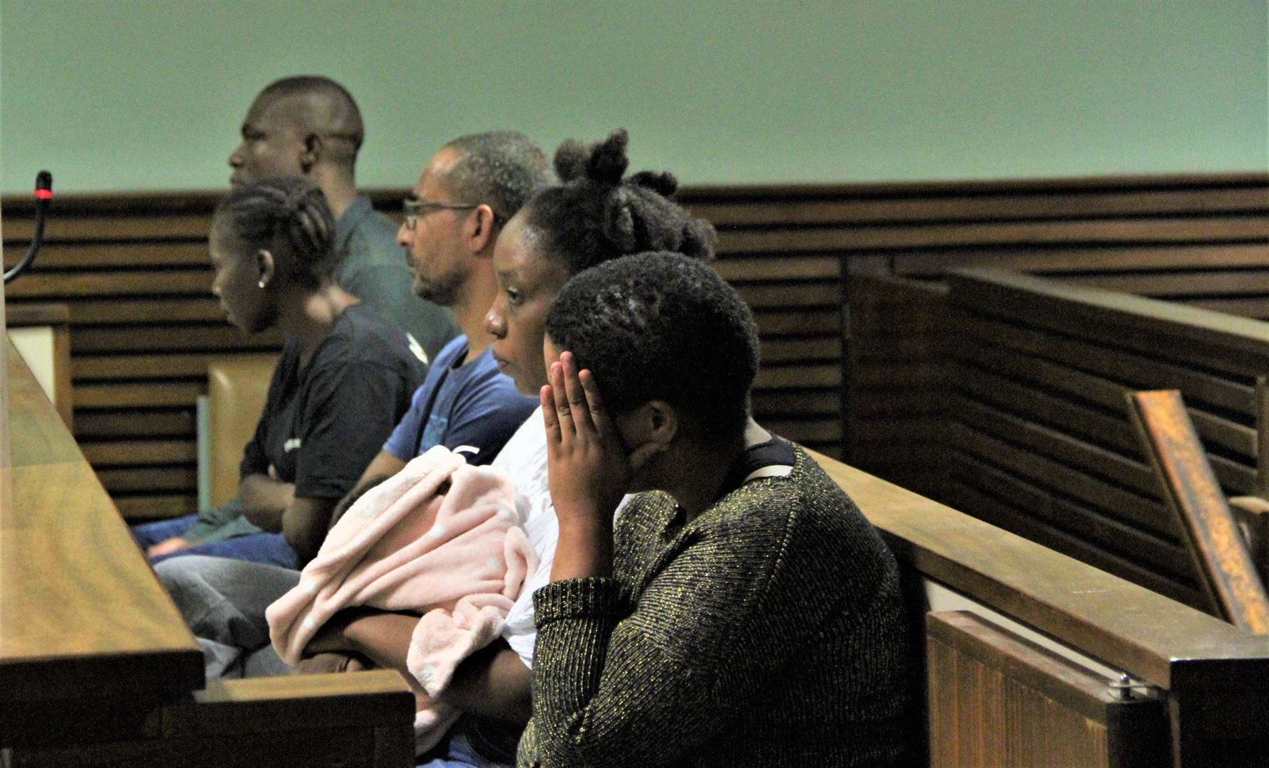 Die beskuldigdes sit op die hofbanke.