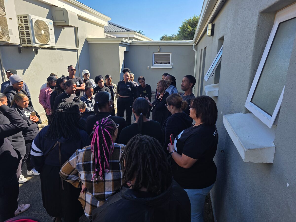 Vroue in Aksie-leier Zorah Motasi spreek mense buite Strand-hof nadat broers borgtog gestaak het.