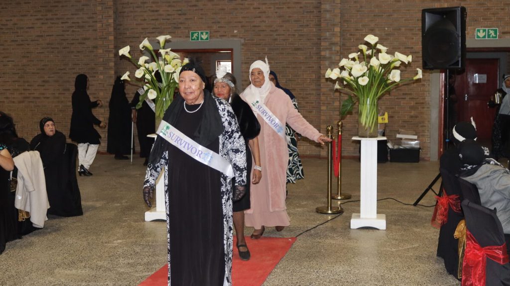 Survivors in shimmering 1920s costumes process down red carpet led by Gaironisah Hendricks.