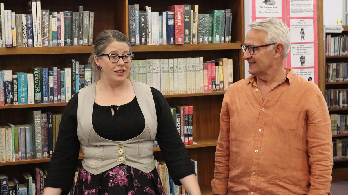 Karen Ellis van die biblioteek verwelkom Frik de Jager wat glimlag en na haar luister by die bekendstelling.