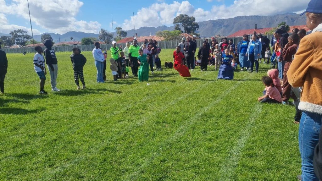 Drie kinders neem deel aan 'n sakresies terwyl toeskouers hulle toejuig by die speletjiesdag.