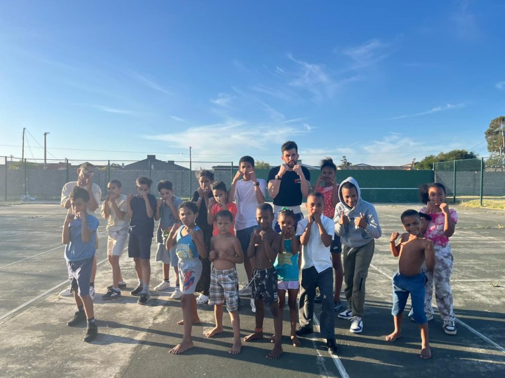 Phillip Cronjé en groep kinders demonstreer bokstegnieke saam op 'n buitensport terrein