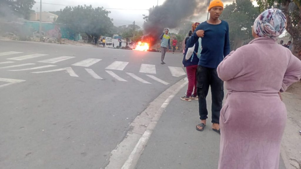 Rayn Mentoor praat met gemeenskapsleier Petrolene Alberts terwyl bande brand op die kruising.