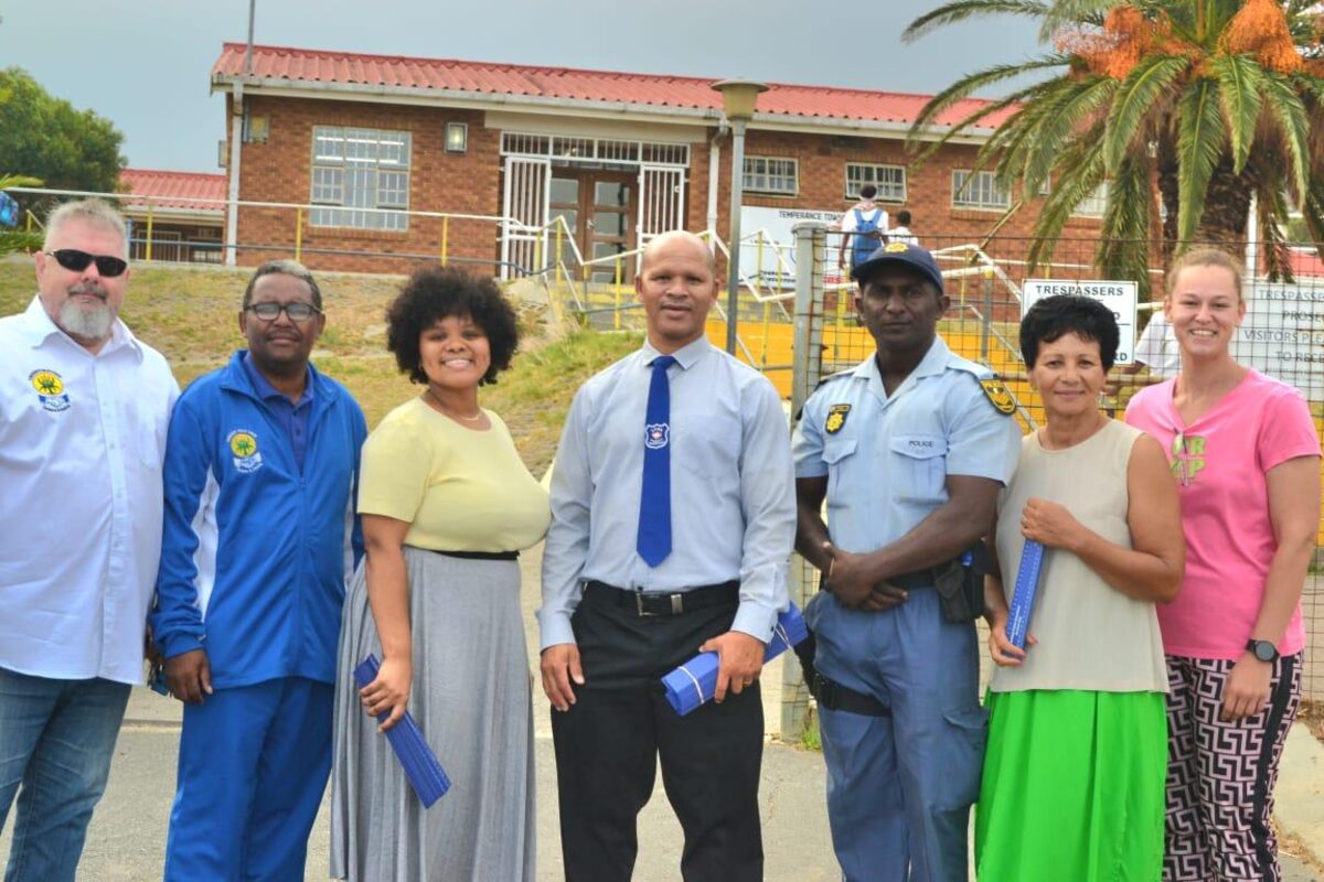 "Seven community leaders and police officers distribute anti-bullying rulers to excited primary school learners