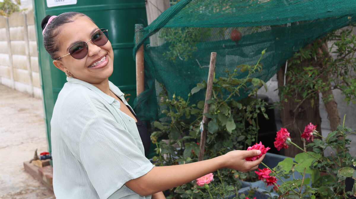 Andrea October werk tussen plante in 'n tuin en raak aan die blare.