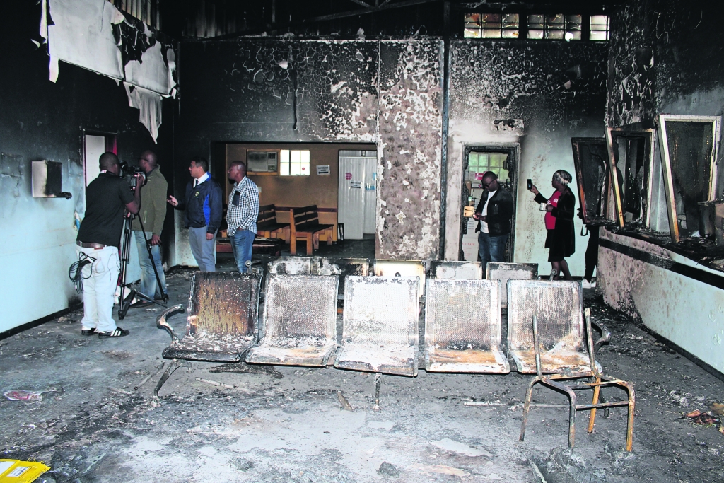 Officials and journalists inspect the petrol-bombed remains of the Ikhwezi Clinic in Lwandle, 2019.