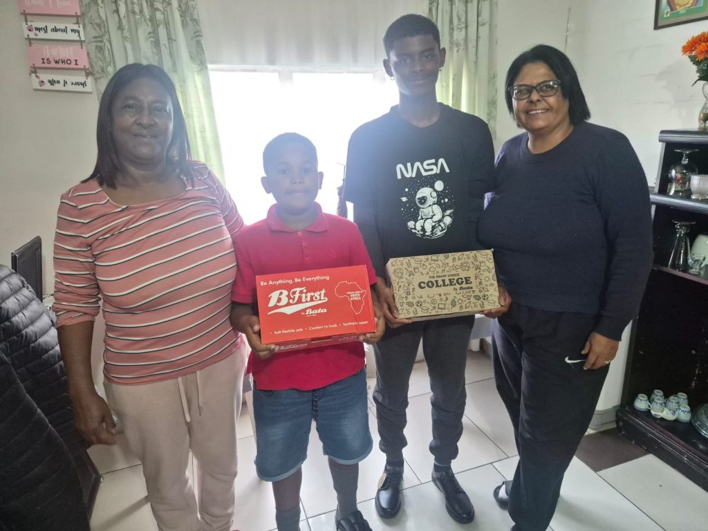 Angela Jantjies and sons Tyrone and Chriswell smile as councillor Chantal Cerfontein hands over shoes.