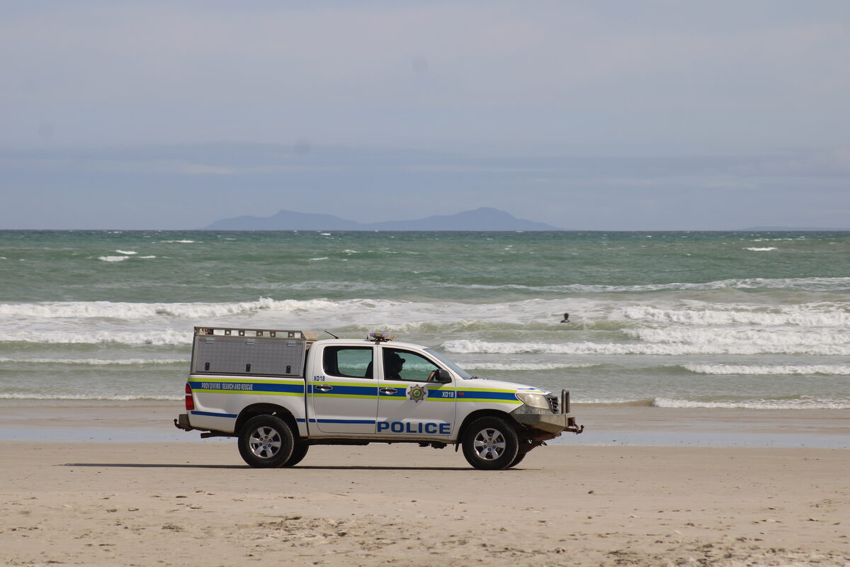 A police vehicle remains on standby at the water’s edge while rescue operations continue in the water.