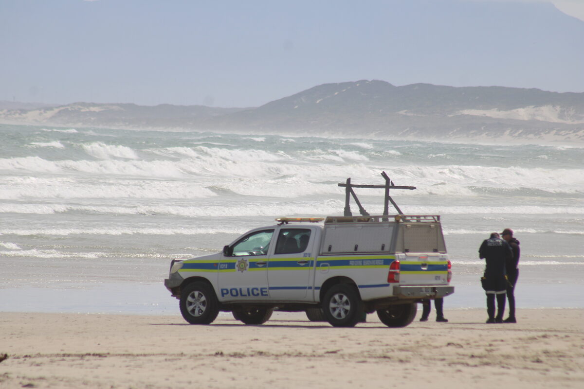 A police search-and-rescue vehicle stays positioned on the beach while officers scan the surf line for any signs of the missing swimmers. 