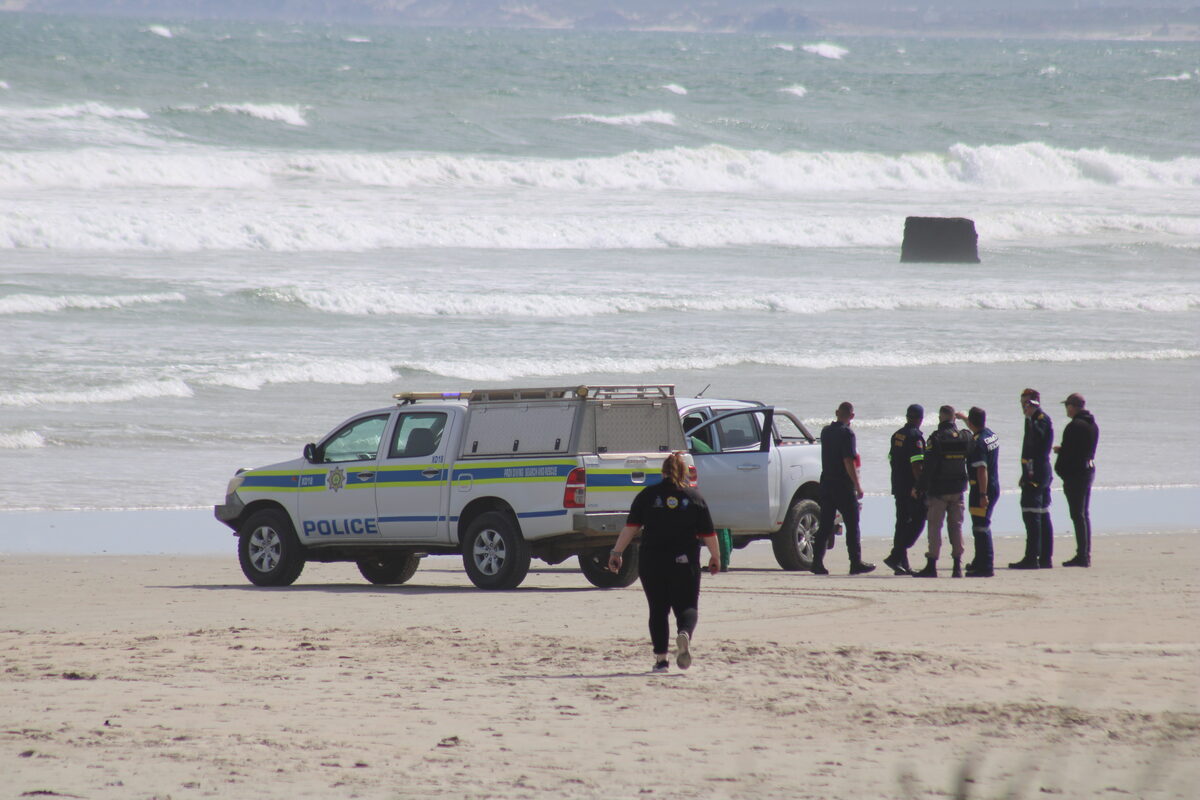 Police officers and emergency personnel gather beside a police response vehicle to coordinate search-and-rescue efforts along the shoreline. Photo: Yaseen Gaffar