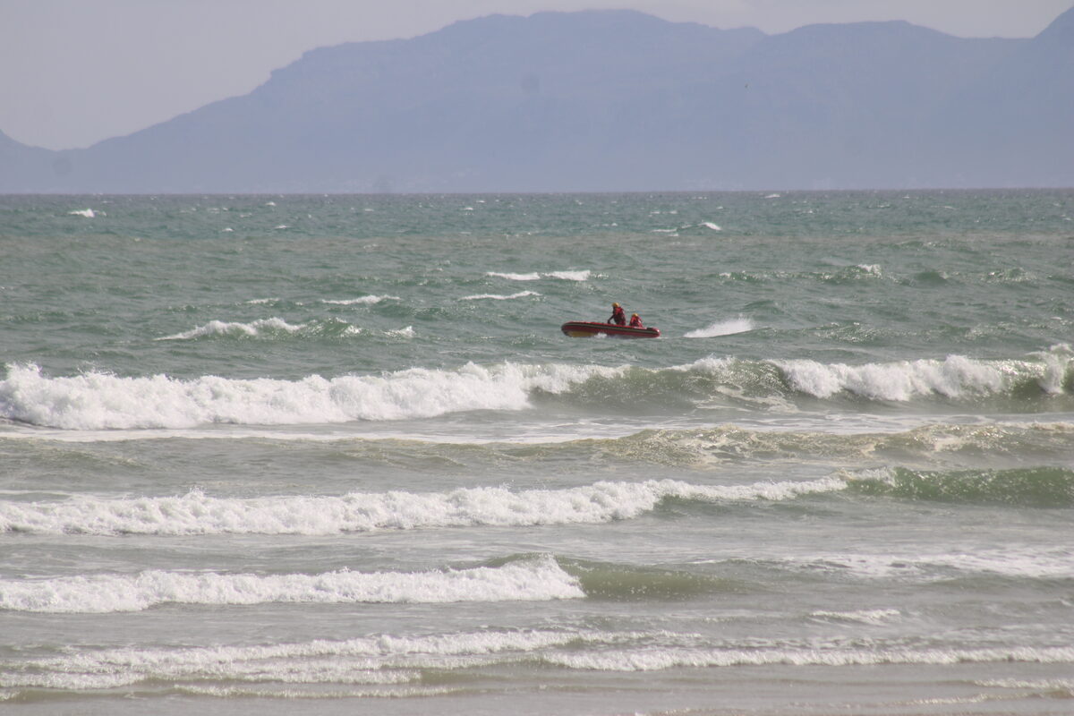 An NSRI rescue craft navigates choppy ocean waters off Strand Beach as crew members search the waves for the two missing swimmers