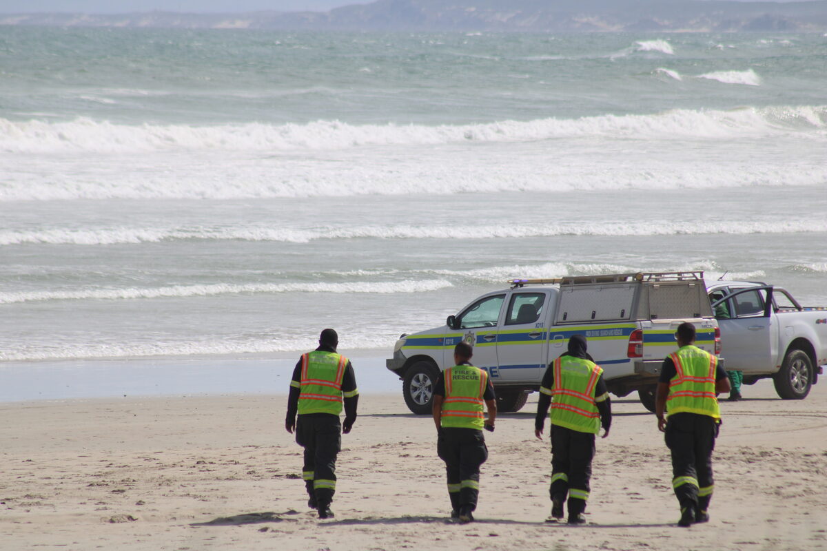 Fire and Rescue Service personnel head across the beach to join emergency teams at the water's edge as search operations intensify. Photo: Yaseen Gaffar