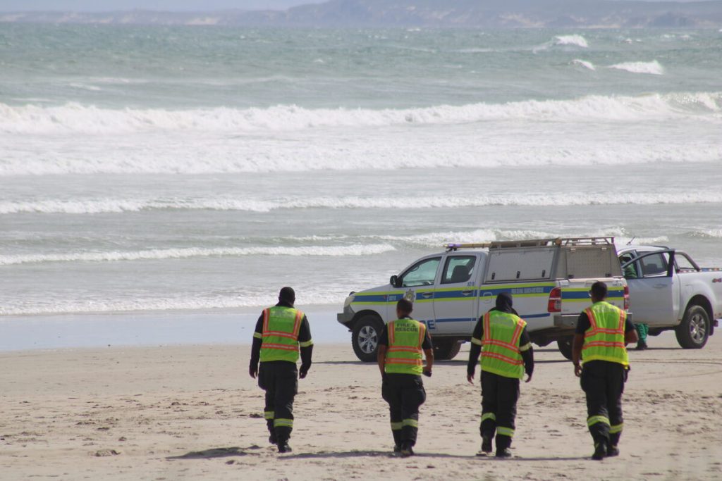 Fire and Rescue Service personnel head across the beach to join emergency teams at the water's edge as search operations intensify. Photo: Yaseen Gaffar