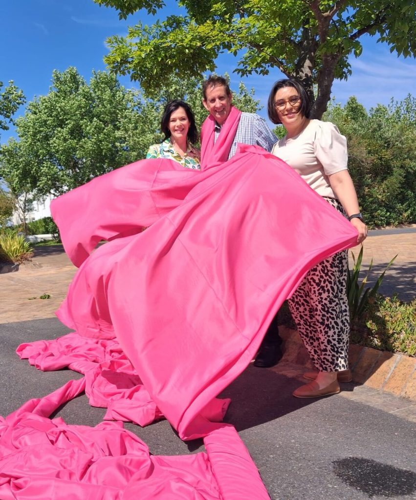 Internationally, October is recognised as Breast Cancer Awareness Month, and this year the De Zalze Winelands Golf 
Estate is proudly participating in this important initiative through a collaboration with Pink Trees for Pauline. Several trees on the estate are wrapped in pink fabric as a visual symbol of solidarity with those affected by cancer – a 
reminder of hope, support and community. As part of the initiative, a donation was also made to the Stellenbosch Hospice to express appreciation for the incredible work it does every day to support patients and their families with dignity and compassion, and the immeasurable difference it makes in their lives. Each pink tree is a beacon, reminding all to stand tall, stay grounded, embrace challenges and keep growing with courage! Adri Jansen van Nieuwenhuizen of Pink Trees for Pauline, Peet de Wet, CEO De Zalze Winelands Golf Estate HOA, and Jennilee Geduld, general manager of Stellenbosch Hospice, helped to make sure the estate lanes are lined in pink.