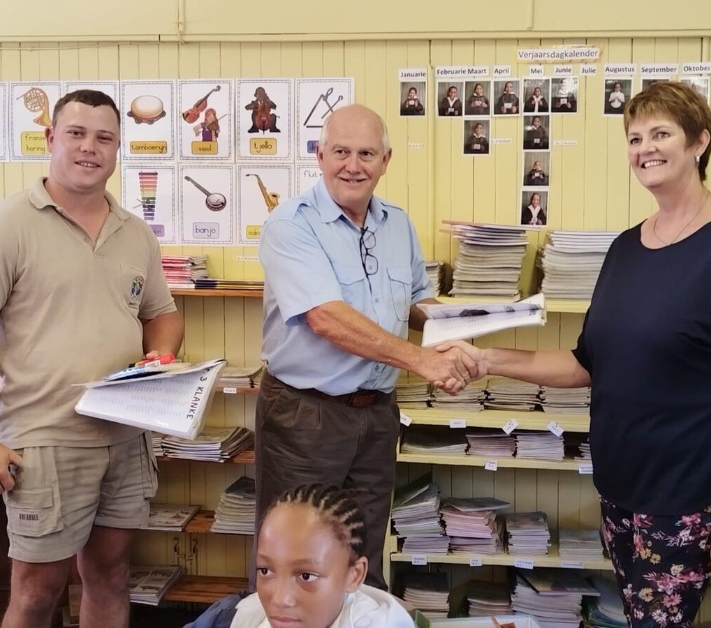 Drie mense wat langs mekaar staan met twee van hulle wat hande skud.