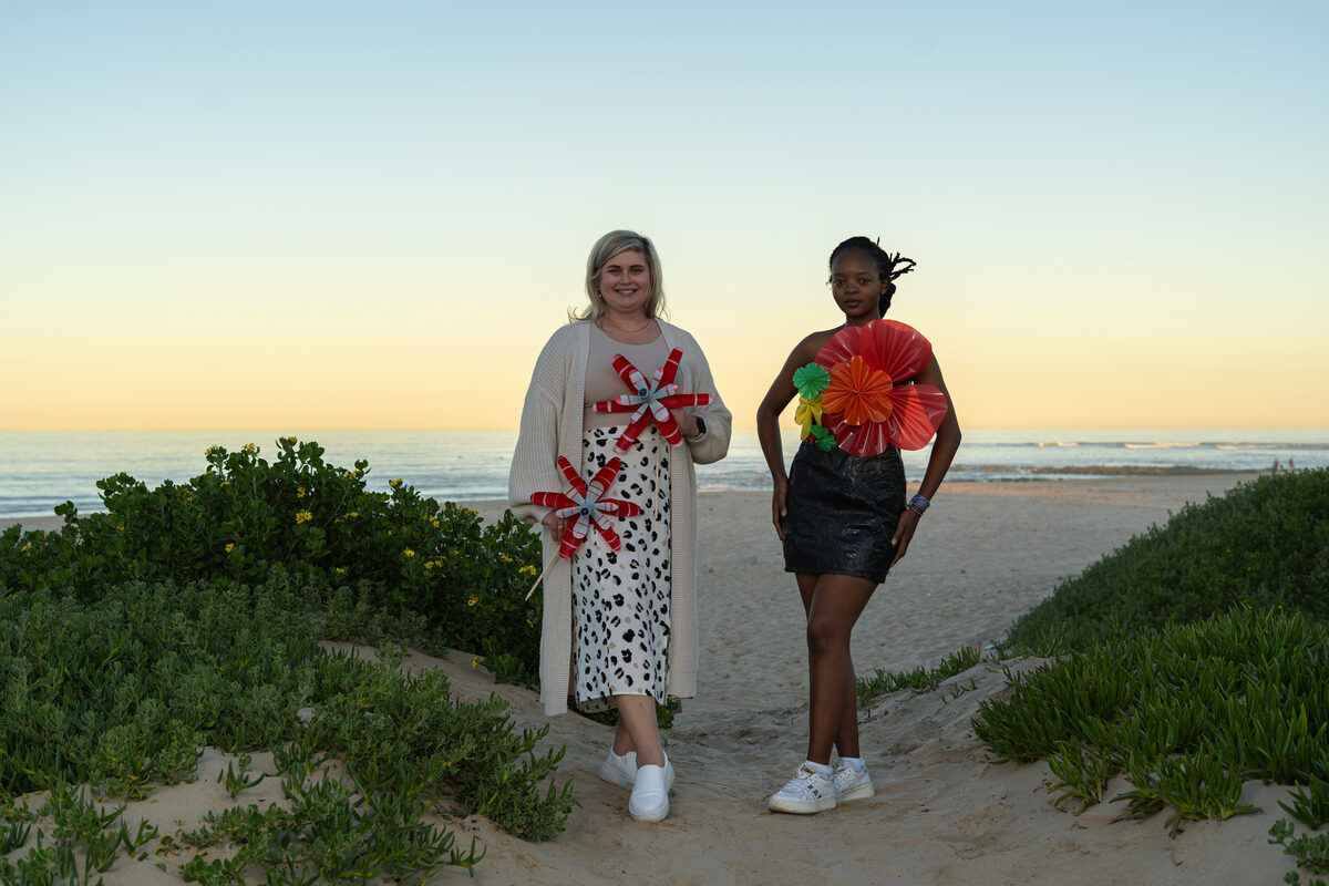 Two women standing on beach sand with the sea as a back drop.