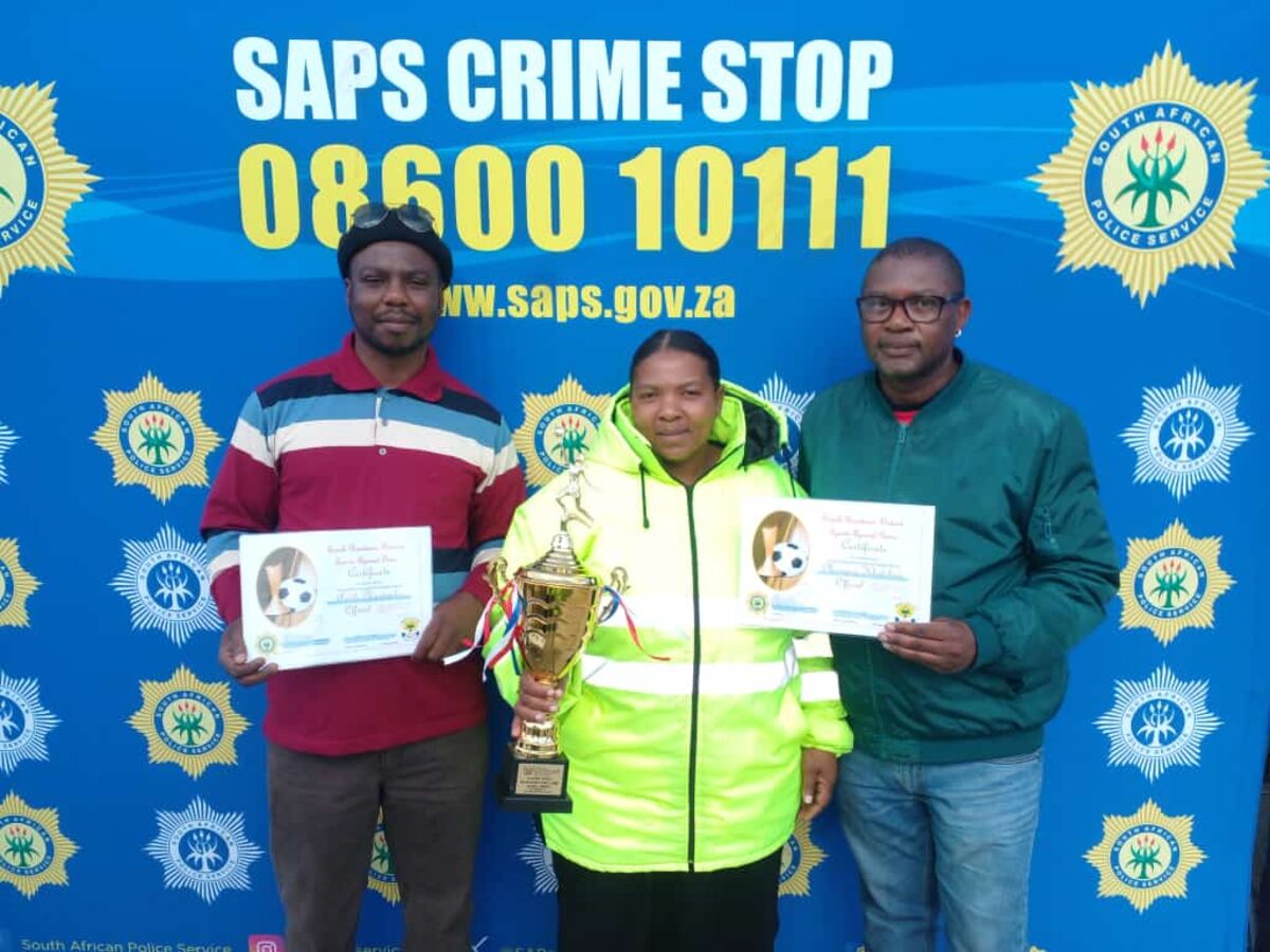 Three people standing with certificates in front of an SAPS poster.
