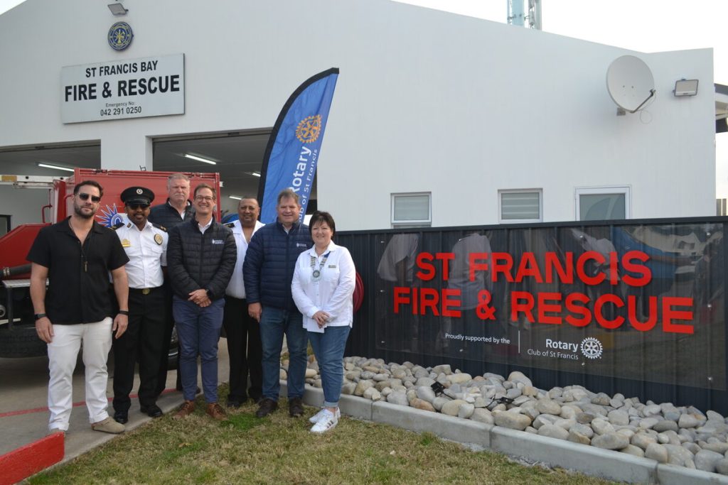 A group of people standing alongside a sign board.