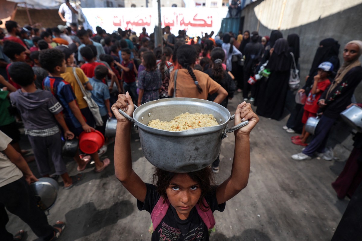 A Palestinian child walks away with a pot of rice obtained from a charity kitchen in the Nuseirat refugee camp in the central Gaza Strip, amid a UN-declared famine after nearly two years of war. (Photo by Eyad Baba / AFP)