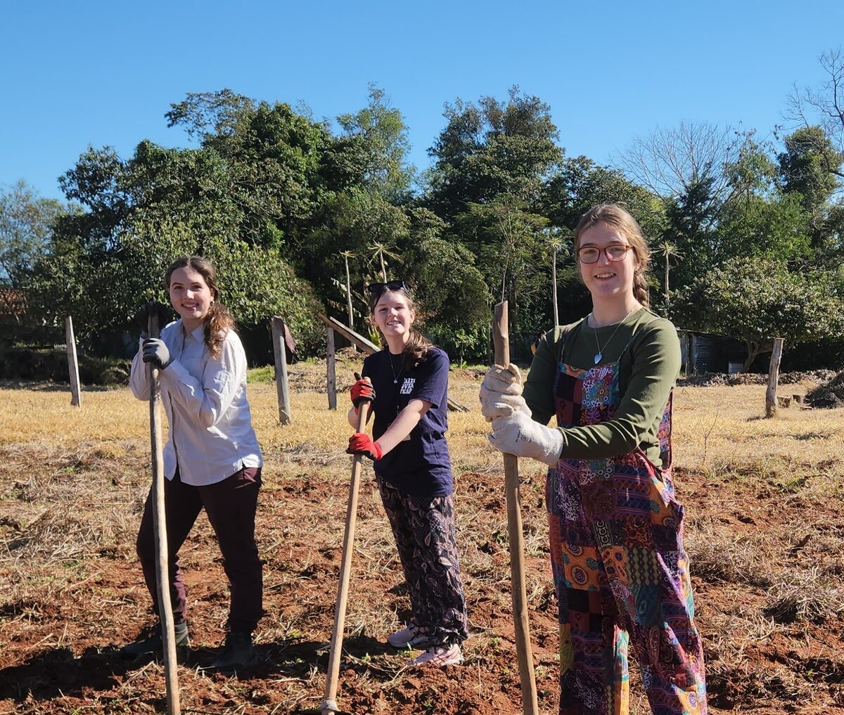 Three learners standing with gardening tools at an empty field.