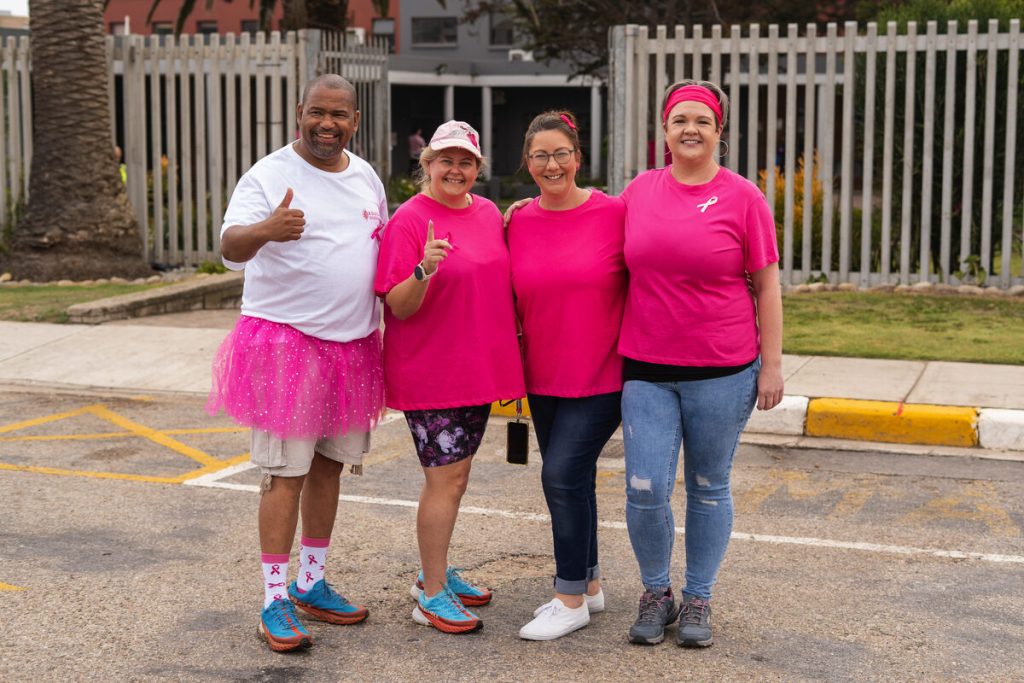 Four people standing alongside each other wearing pink and white t-shirts.