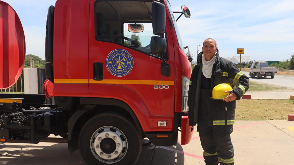 Kouga firefighter Benito Wabanie in front of a fire truck.