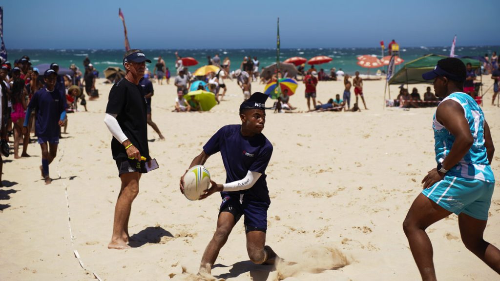A group of people play touch rugby on the beach.