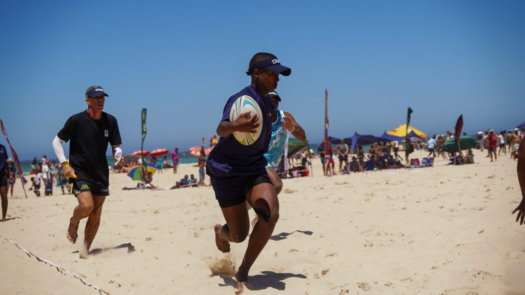 A group of people play touch rugby on the beach.