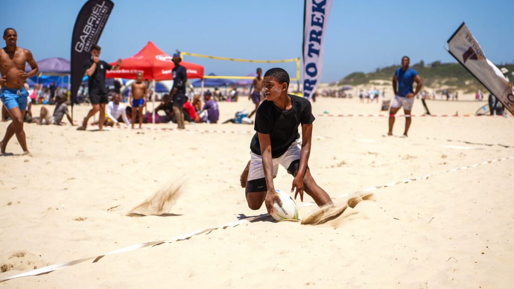 A group of people play touch rugby on the beach.
