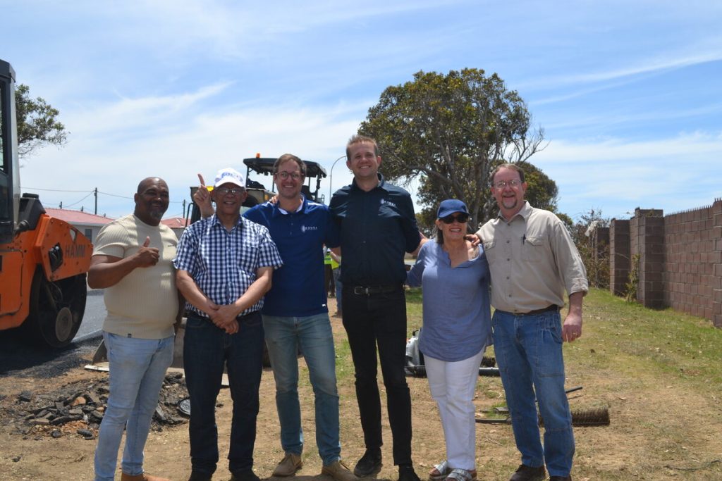 A group of people standing a long side each other with heavy construction equipment behind them.