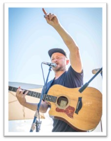 Nick Turner with a guitar singing into a microphone.