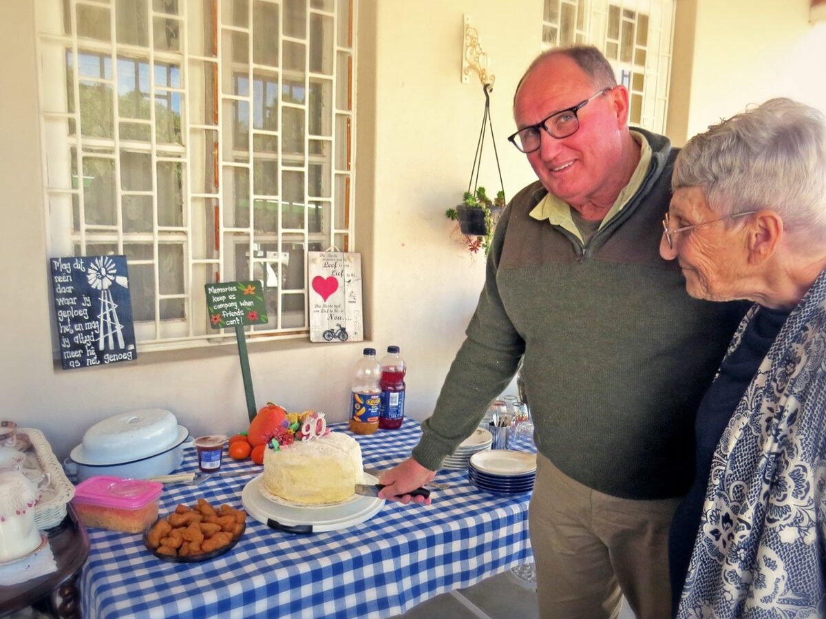 Hannes Papenfus, bestuurder Kokerboom-Oord, sny die verjaarsdagskoek terwyl Hannie Pretorius toekyk.