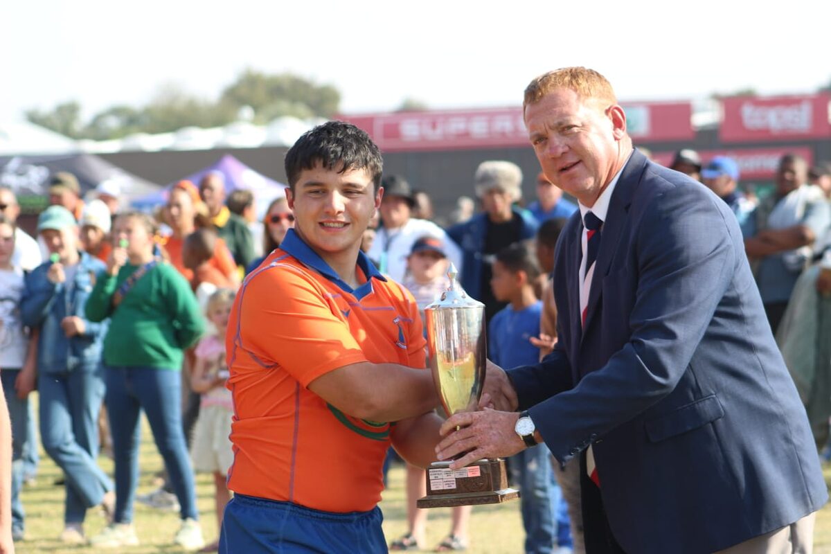 Juvan Stander, kaptein van Uppies se o.19A-span, ontvang die beker van dr. Rooies Adrianatos, skool van Duineveld.
