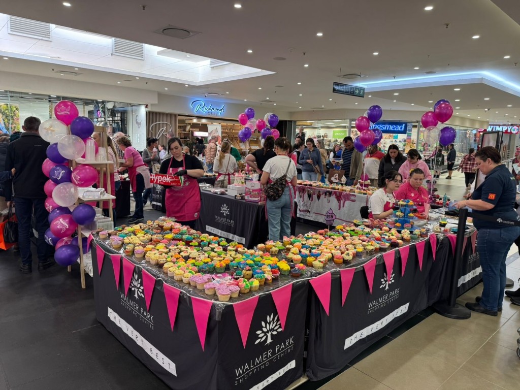 A table filled with cupcakes and a large group of people surrounding the tables.