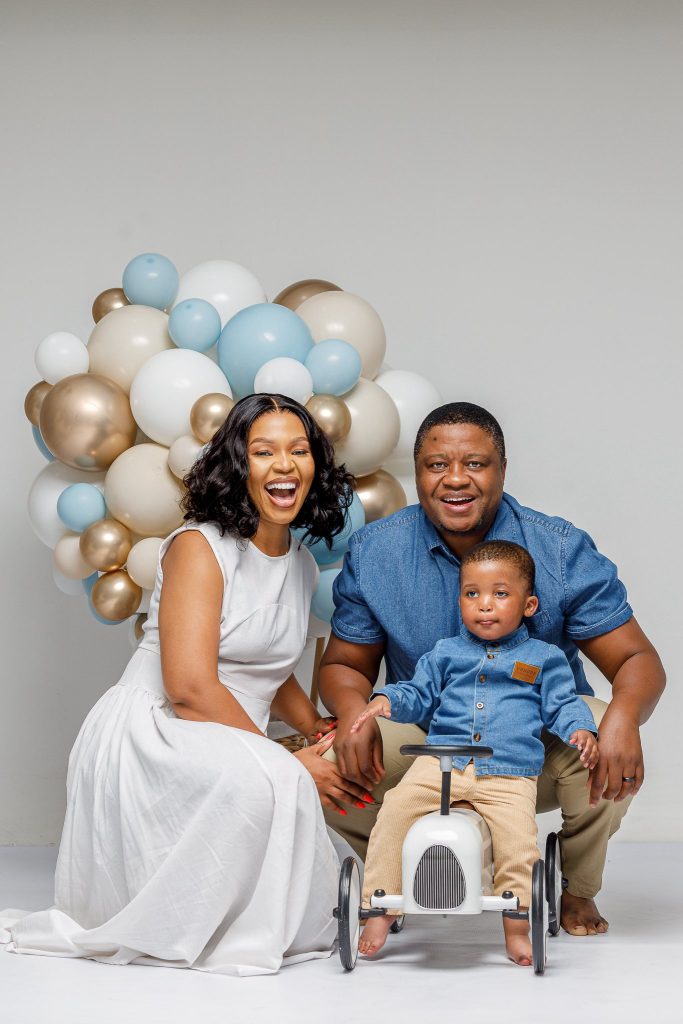 Nozibele Qamngana-Mayaba with her husband and child, smiling and standing together in a family portrait.