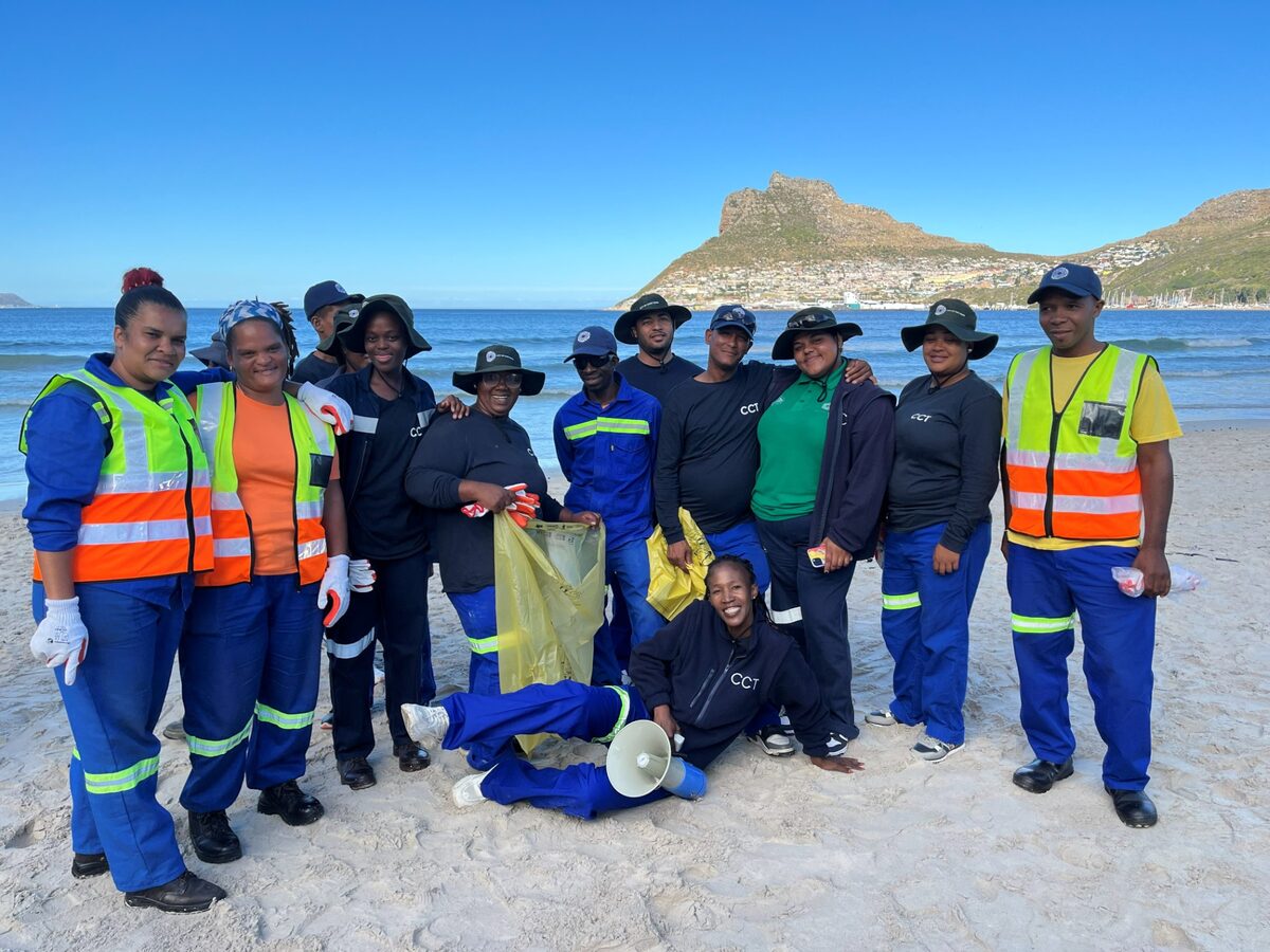 Volunteers collecting litter during a beach clean-up in Hout Bay, Cape Town, with focus on removing plastic waste and raising awareness about environmental pollution.