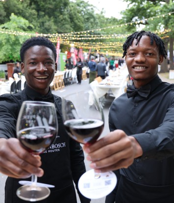 Prosper Kasina en Felix Rukuni verwelkom gaste by die Langtafel met ’n glas Stellenbosch-wyn. Ledeplase van Stellenbosch Wynroetes – wat vanjaar sy 55ste verjaardag vier – het die wyn vir die aand se fees geborg. Foto: Clifford Roberts