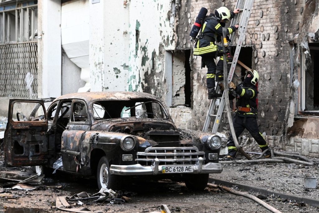 Firefighters are seen next to a burnt-out car following mass Russian drone and missile strikes in the western Ukrainian city of Lviv.