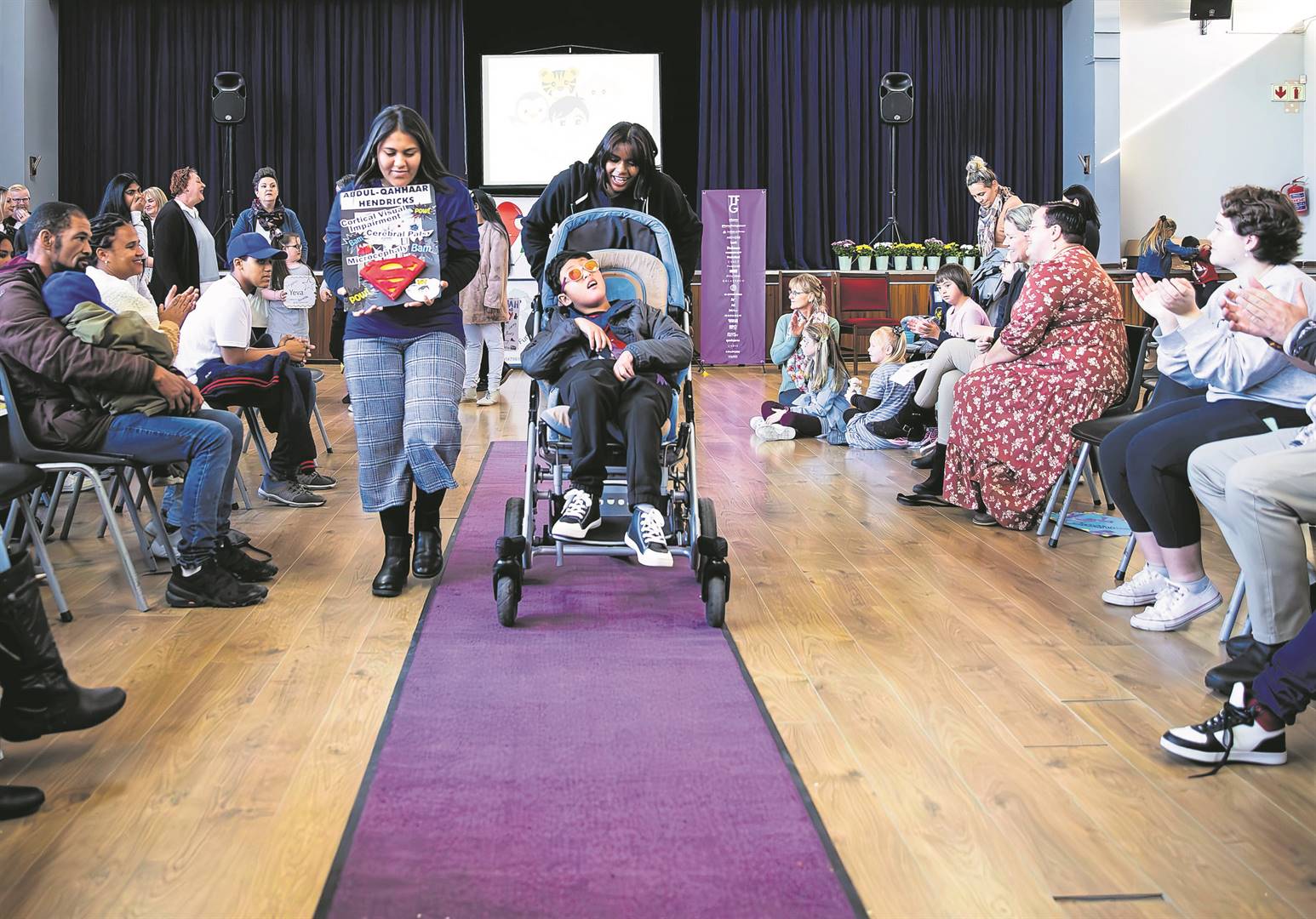 Little boy assisted by family members down catwalk