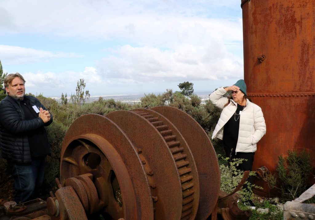 Charles Lourens, assistant winemaker and Denise Johnson, owner of Zevenwacht at the steam-powered winch used to lower men down the shaft and a coal-fired boiler, remnants from tin mining activities on the estate in the early 1900s.