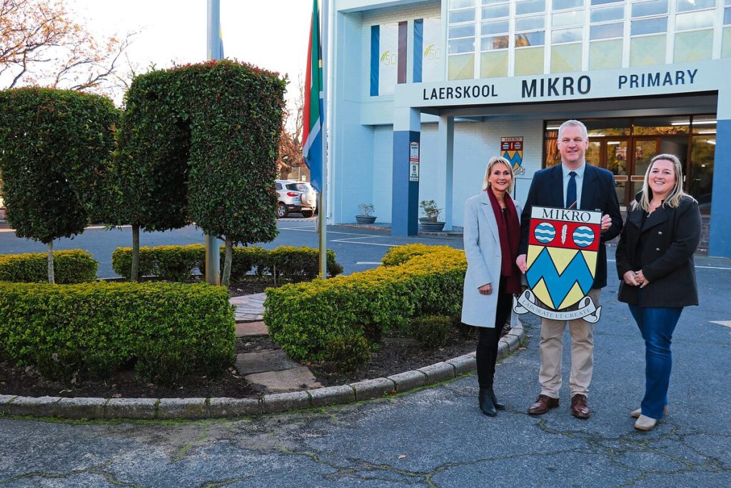 Van links is Annerie Spreeth (adjunkhoof), Louis Mouton (skoolhoof) en Stephanie Burgess (beheerliggaamvoorsitter) met die Laerskool Mikro se skoolwapen met die skoolleuse nou in Latyns" "Laborate Et Create".