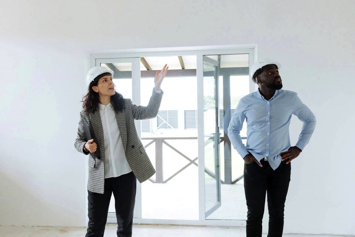 A stock image of two people dressed formally and waring hard hats inspecting and empty building.